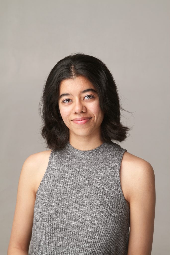 Photograph of Divija Madhani, a dark-haired woman with a warm smile wearing a professional grey dress.